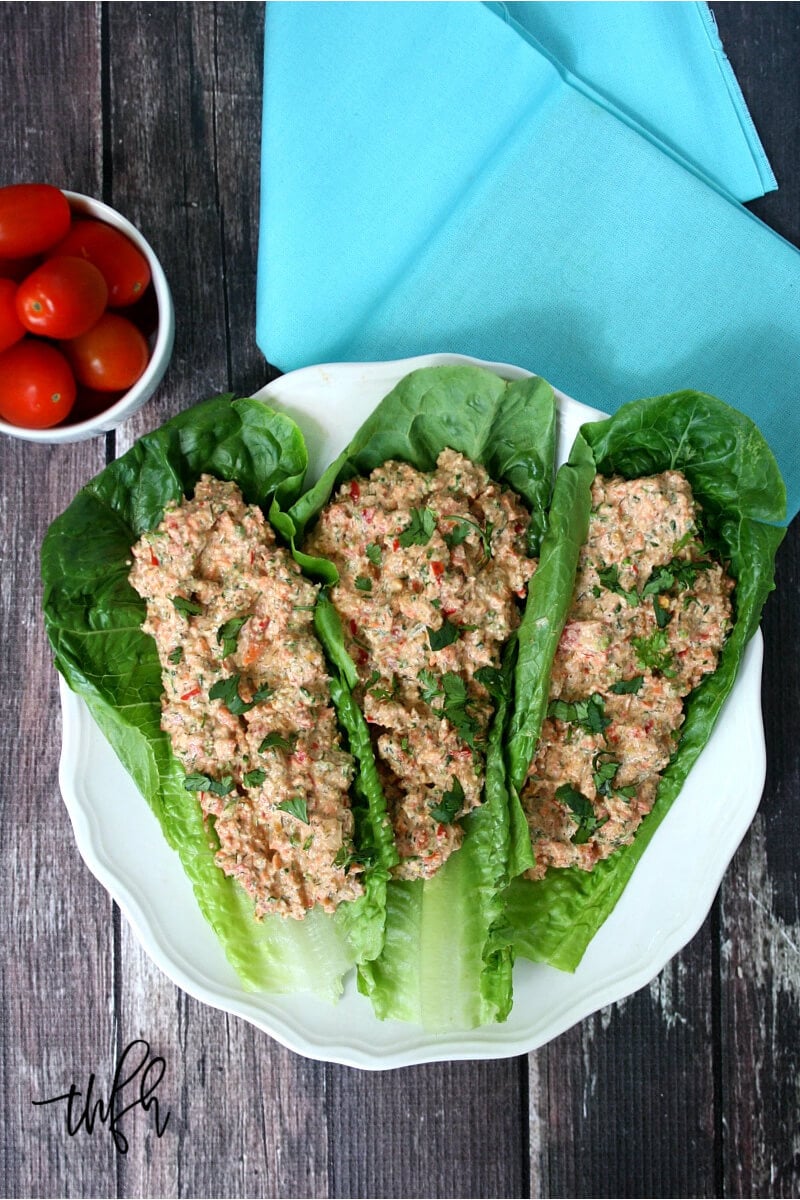 Three romaine lettuce leaves filled with The ORIGINAL Raw Mock Vegan "Chicken" Salad on a white plate on a wooden surface