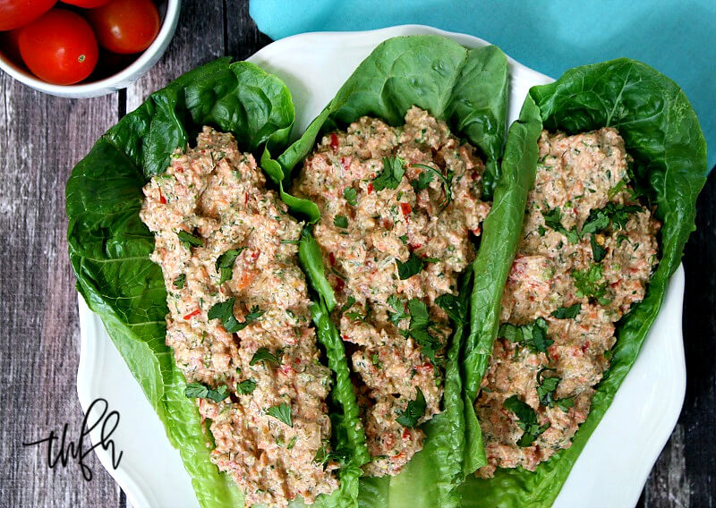 Horizontal image of three romaine lettuce leaves filled with The ORIGINAL Raw Mock Vegan "Chicken" Salad on a white plate on a wooden surface