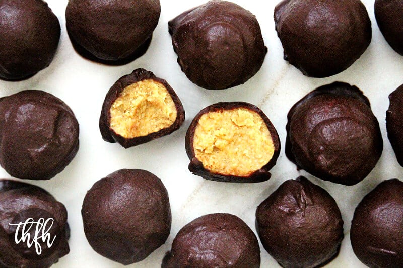 Overhead horizontal view of Healthy Gluten-Free Vegan Peanut Butter Bon Bons (aka Reese's Vegan Peanut Butter Eggs) showing the inside of one cut open on a white marble surface