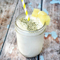A mason jar filled with Pineapple and Banana Hemp Smoothie garnished with pineapple chunks and straw on a weathered wooden surface