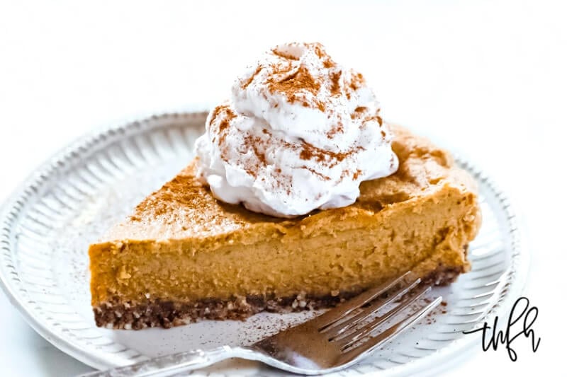 Horizontal image of a slice of Gluten-Free Vegan No-Bake Pumpkin Pie on a decorative grey plate next to a silver fork with a large dollop of vegan whipped cream on top