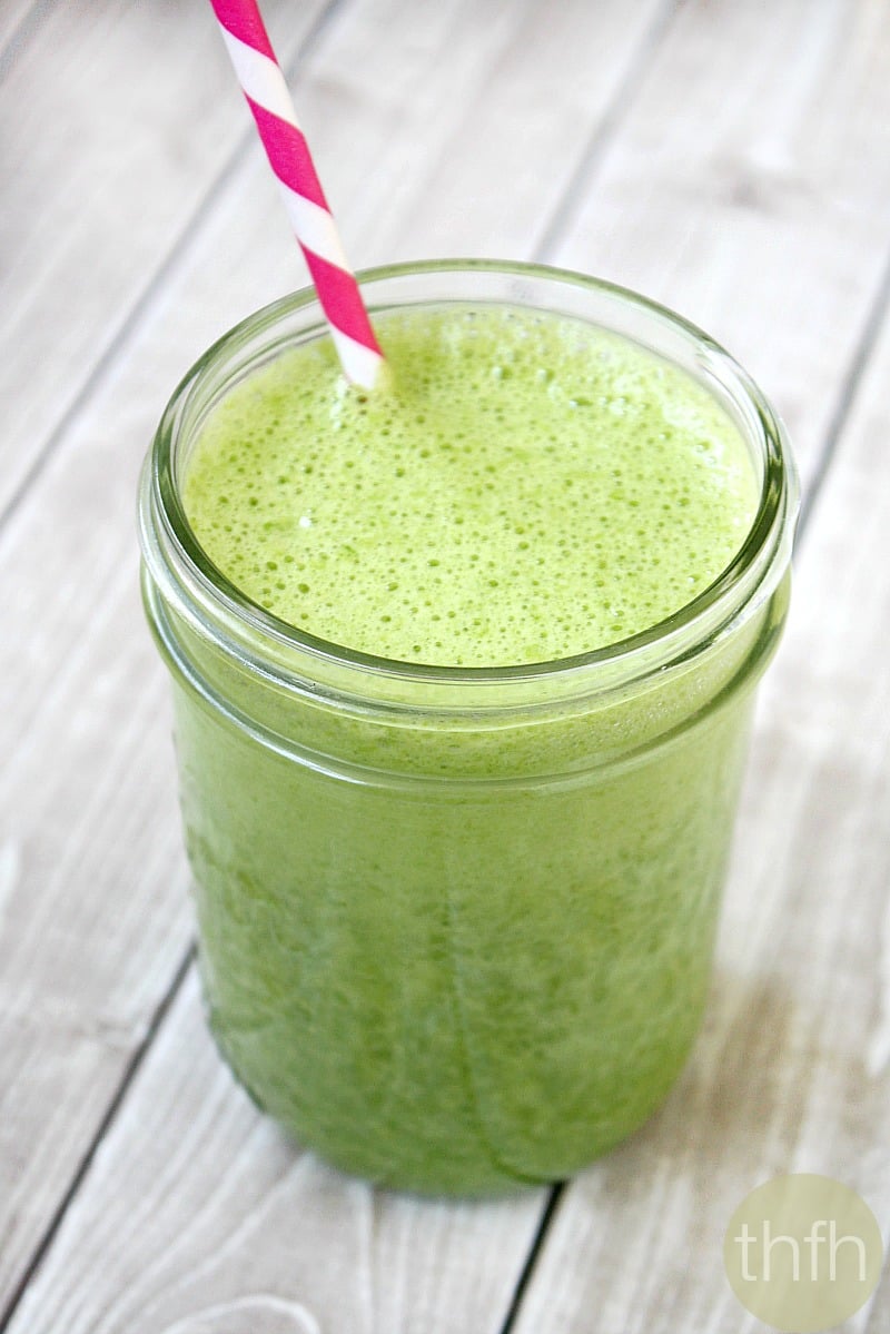 Vertical image of a glass mason jar filled with Kale and Banana Green Smoothie with a pink and white straw inserted on top of a weathered wooden surface