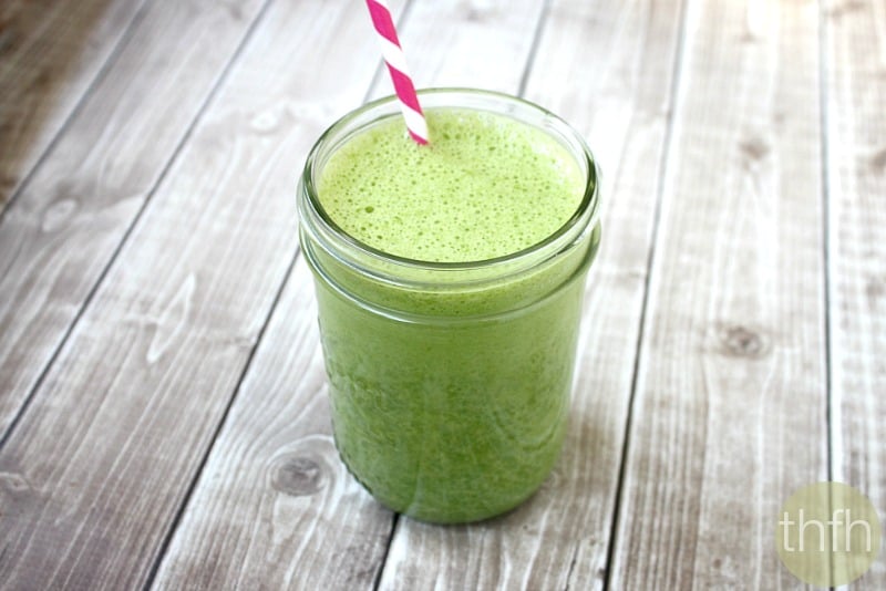 A glass mason jar filled with a Kale and Banana Green Smoothie with a pink and white straw inserted on a weathered wooden surface