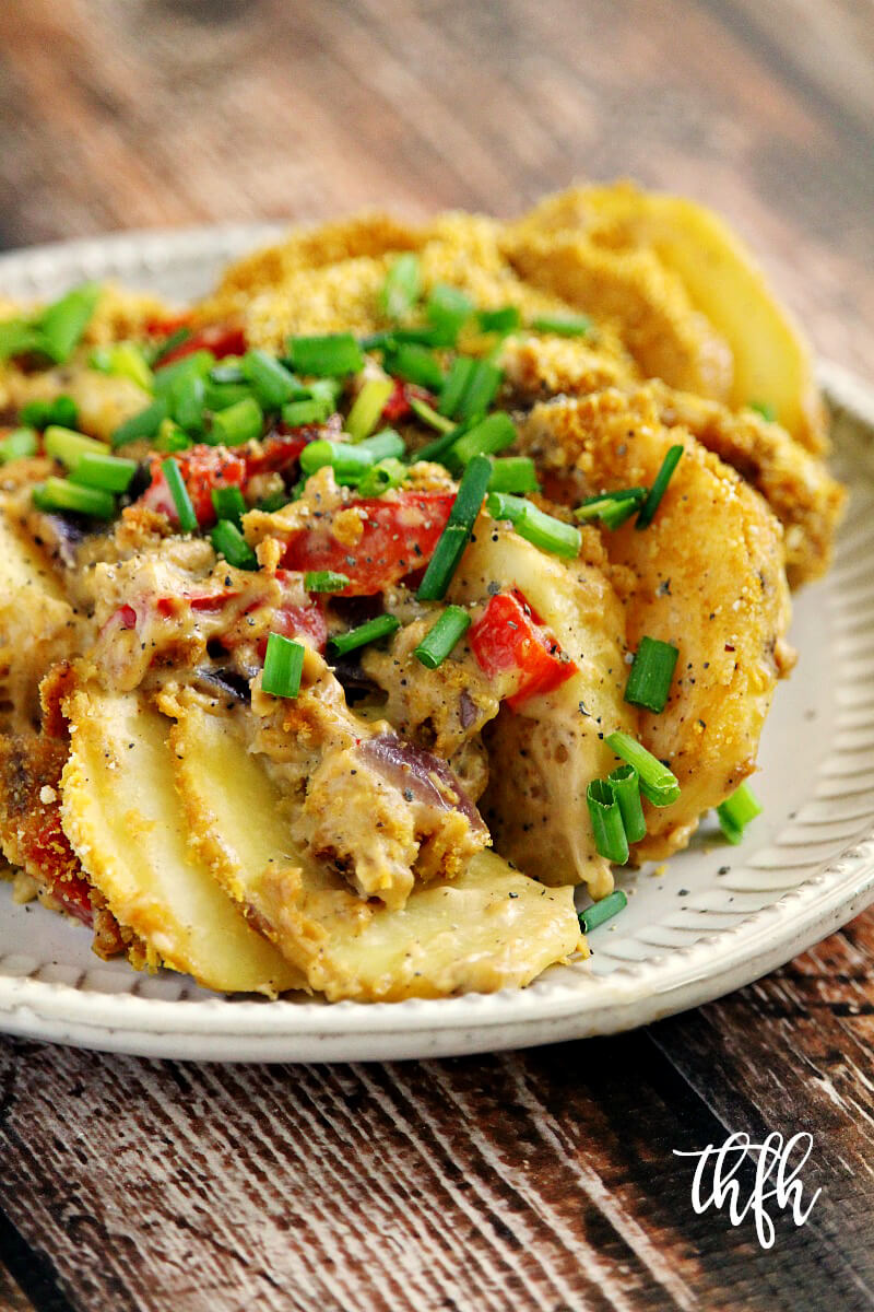 Vertical image of a decorative grey plate filled with Gluten-Free Vegan Potatoes Au Gratin on a weathered wooden surface