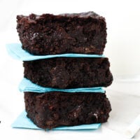 Close up image of a stack of three of The BEST Gluten-Free Vegan Flourless Zucchini Brownies between aqua napkins on a white surface