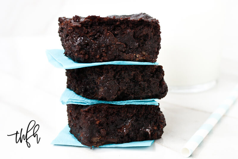 Close up image of a stack of three of The BEST Gluten-Free Vegan Flourless Zucchini Brownies between aqua napkins on a white surface