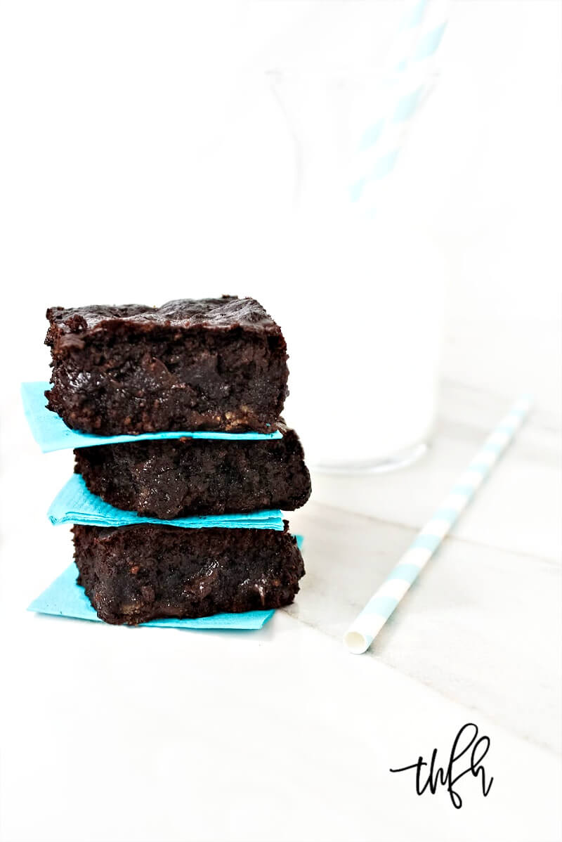Three of The BEST Gluten-Free Vegan Flourless Zucchini Brownies stacked on top of each other with a glass of milk in the background