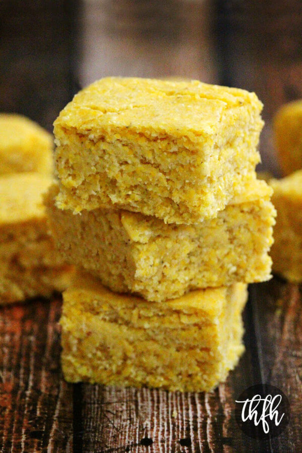 Close-up image of a stack of three sliced squares of The BEST Homemade Vegan Cornbread on a weathered wooden surface