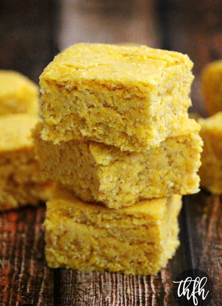 Close-up image of a stack of three sliced squares of The BEST Homemade Vegan Cornbread on a weathered wooden surface