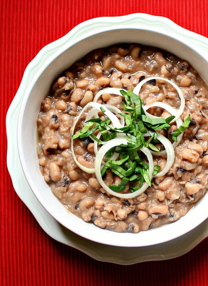 Overhead image of a white bowl filled with Gluten-Free Vegan Instant Pot Black-Eyed Peas on a red cloth surface