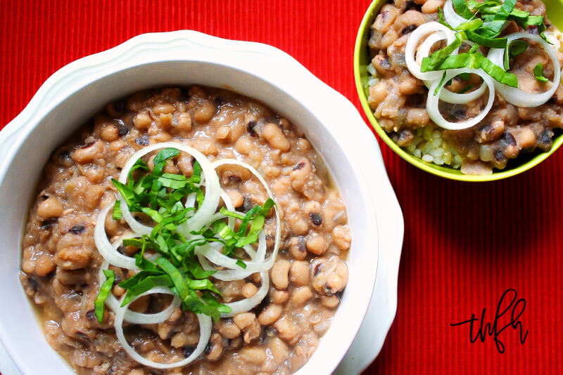 Horizontal overhead view of a large white bowl and small yellow bowl filled with Gluten-Free Vegan Instant Pot Black-Eyed Peas on a red background