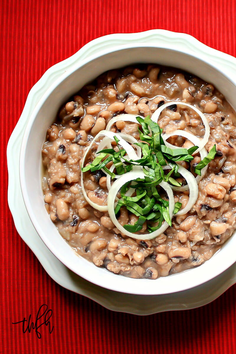 Overhead image of a white bowl filled with Gluten-Free Vegan Instant Pot Black-Eyed Peas on a red cloth surface