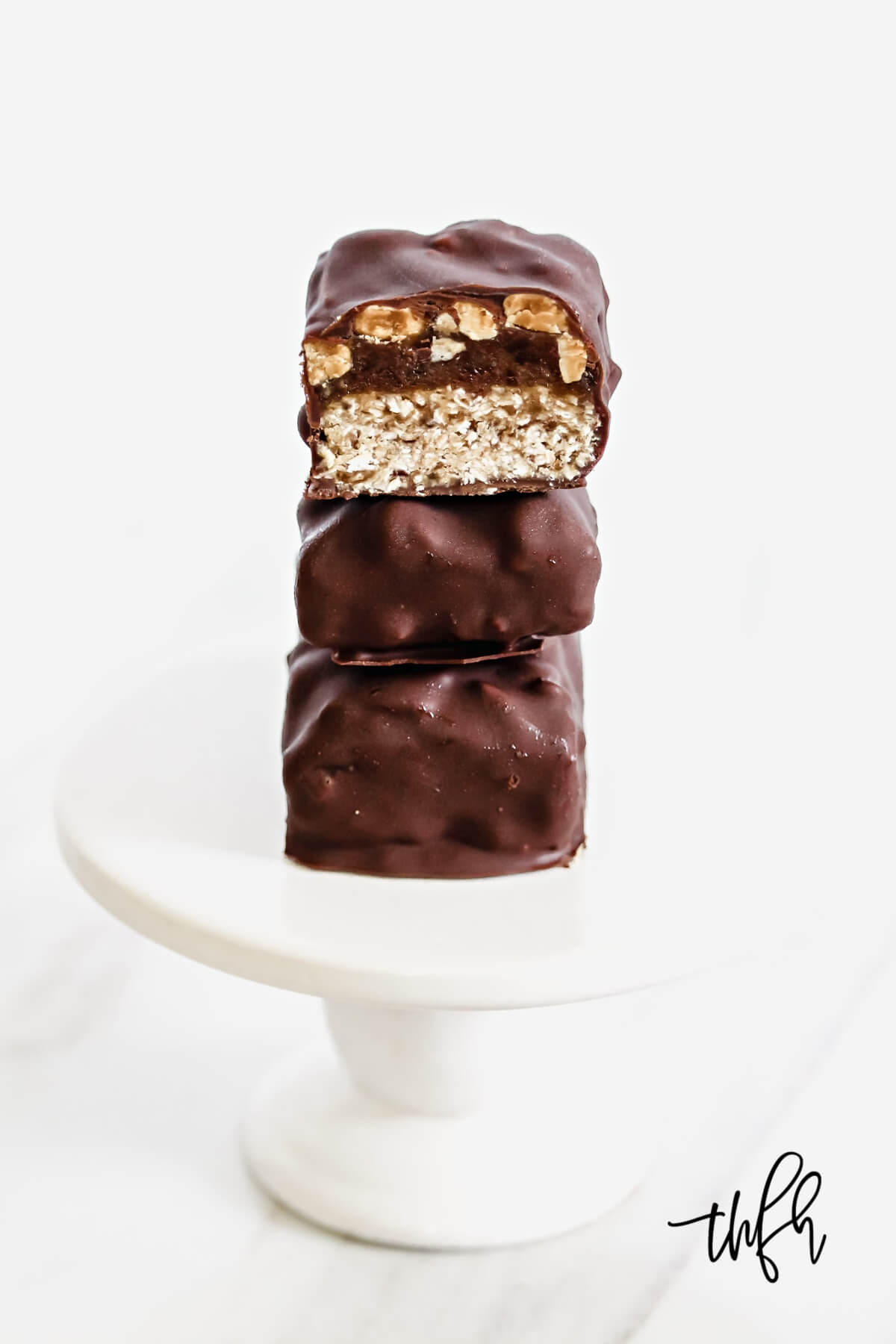 Vertical image of a stack of three homemade snickers bars on a small white pedestal