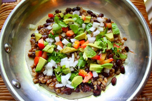 Tortilla topped with ingredients to make black bean quesadillas in a stainless steel skillet
