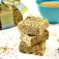 Horizontal image of a stack of three Gluten-Free Vegan No-Bake Hemp and Chia Seed Bars on a white surface with hemp seeds scattered around them