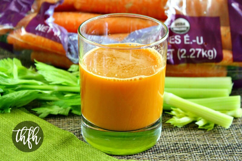 Glass of Healthy Homemade Carrot Apple and Celery Juice with raw carrots and celery in the background