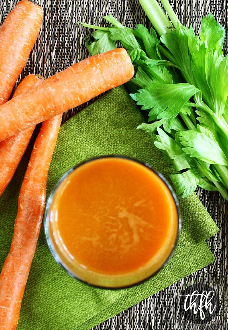Overhead view of a glass of Healthy Homemade Carrot Apple and Celery Juice on a green napkin with raw carrots and celery next to it