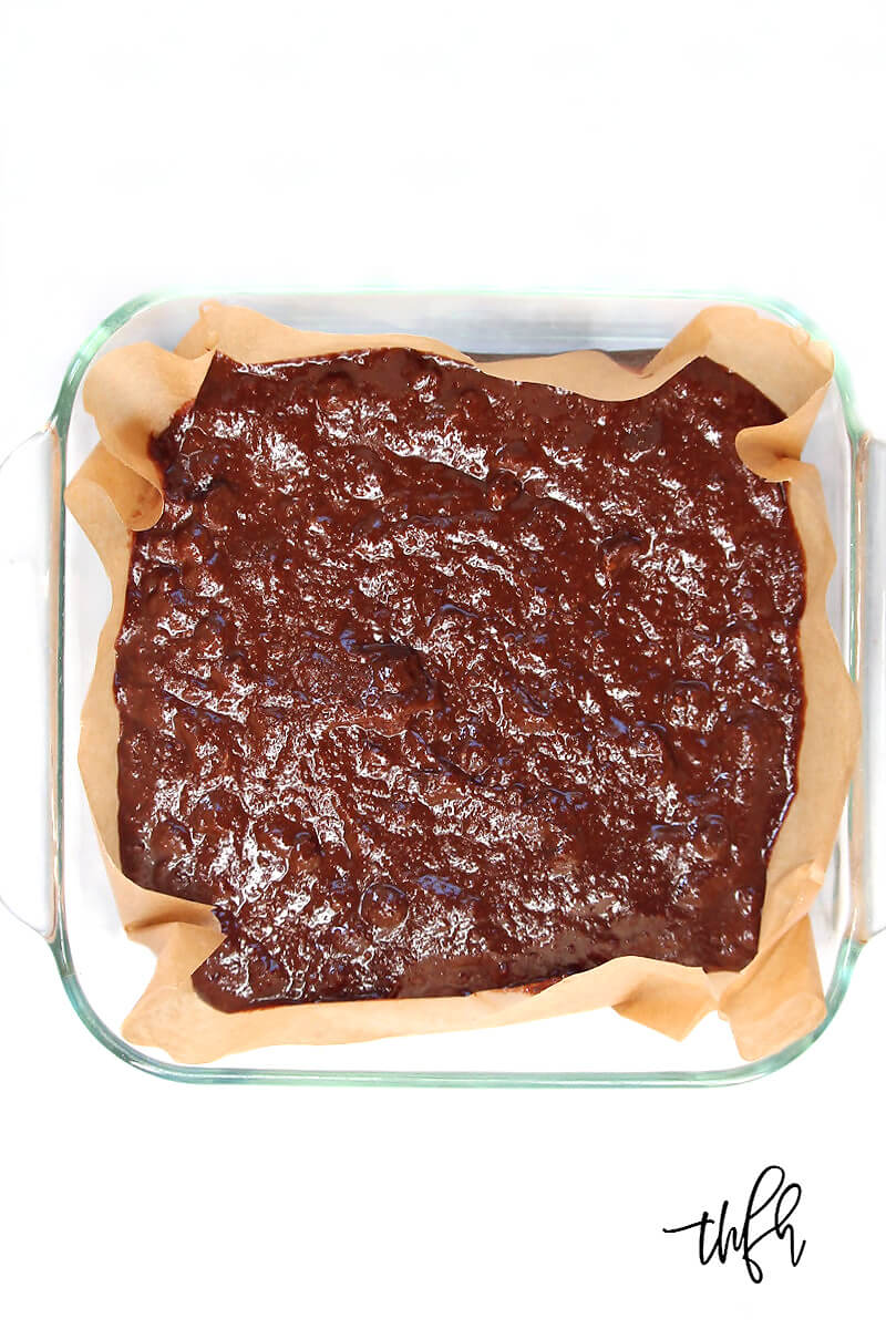 Overhead view of an 8 x 8 glass baking dish of Gluten-Free Vegan Flourless Peanut Butter Swirl Brownies batter on a white surface