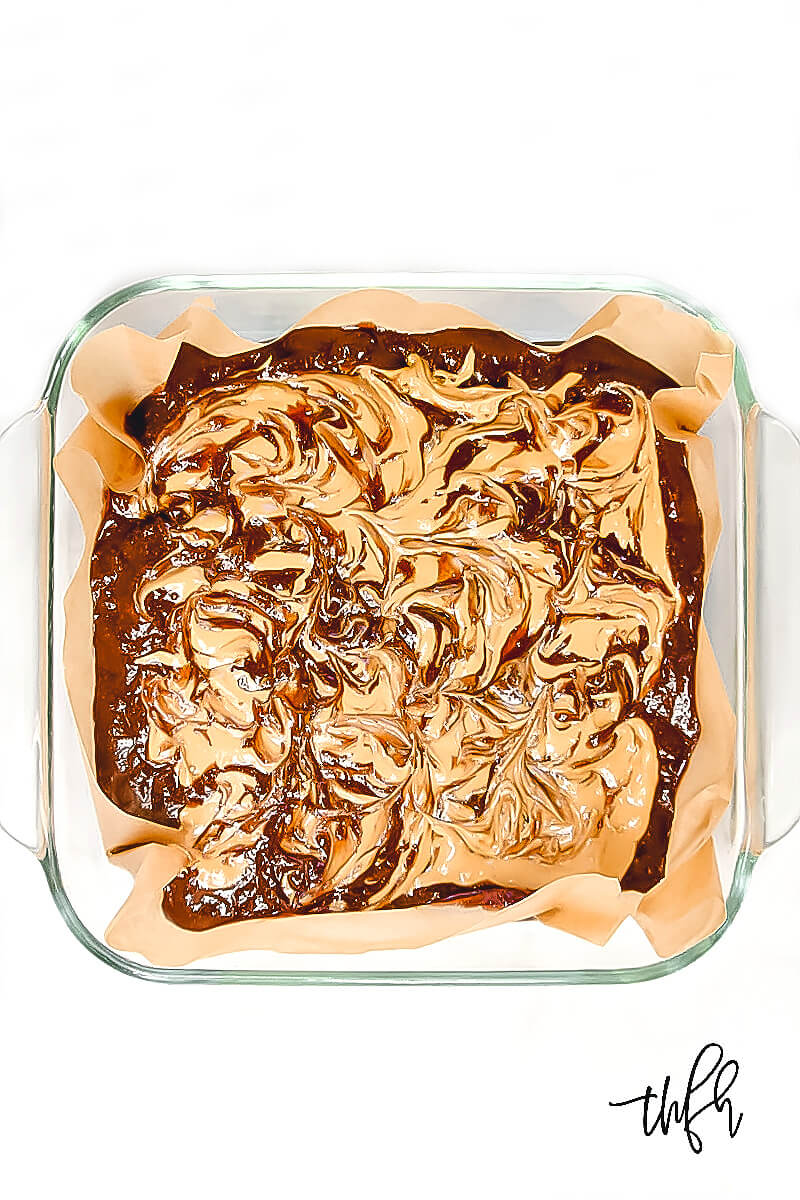 Overhead view of an 8 x 8 glass baking dish with unbaked Gluten-Free Vegan Flourless Peanut Butter Swirl Fudgy Brownie mixture on a white surface