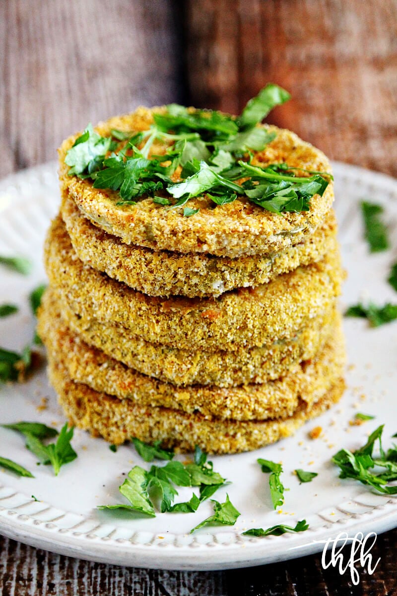Vertical image of The BEST Gluten-Free Vegan Healthy Oven-Baked "Fried" Green Tomatoes on a white plate on a wooden surface