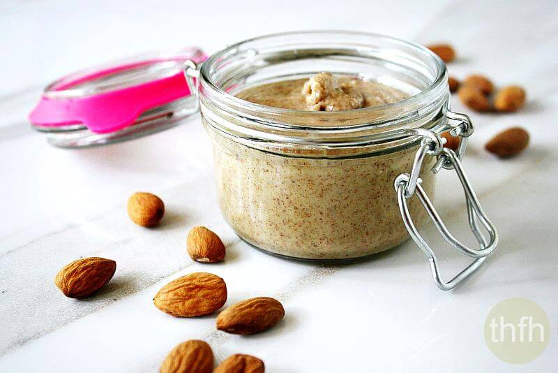 A small glass jar filled with homemade almond butter on a white marbled surface