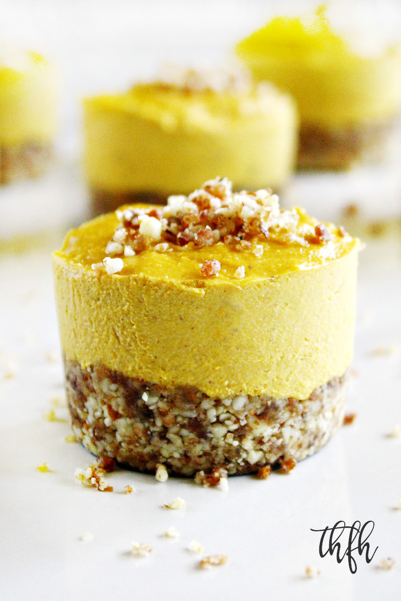 Vertical close-up image of an individual Gluten-Free Vegan No-Bake Pumpkin Mini Cheesecake with crumbles on top and more cheesecakes in the background