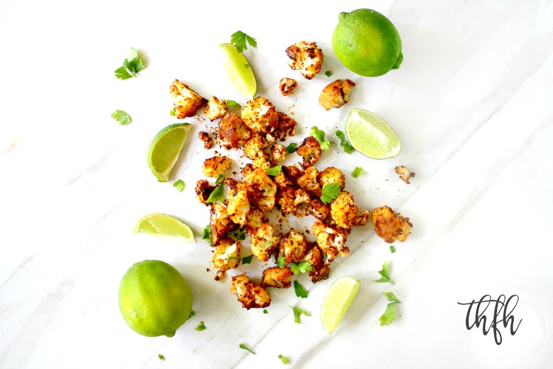 Overhead horizontal view of Gluten-Free Vegan Roasted Cauliflower with Chipotle and Lime scattered over a white marble surface with sliced limes