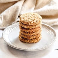 Horizontal image of a stack of Gluten-Free Vegan Flourless Coconut Cashew Cookies on a white plate on a white background
