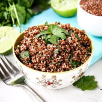 Horizontal image of a small decorative bowl filled with Red Quinoa with Cilantro and Lime next to a fork and squeezed limes to the side