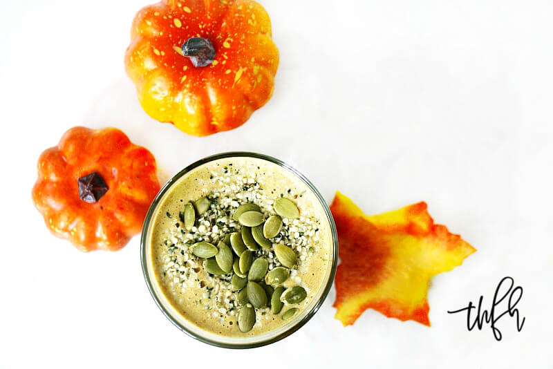 Overhead image of a glass filled with The BEST Vegan Pumpkin Protein Smoothie surrounded by two small pumpkins on a white marble surface