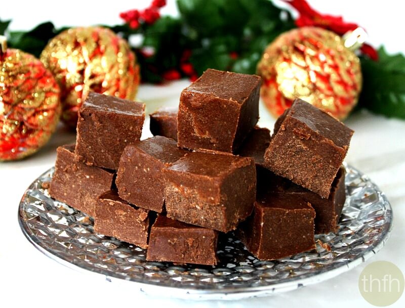 Silver plate with squares of Gluten-Free Vegan No-Cook Healthy Holiday Fudge on a white marble surface with Christmas decorations in the background