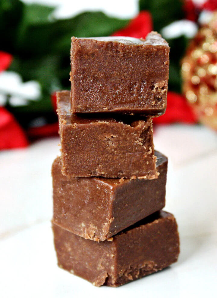Stack of 4 Gluten-Free Vegan No-Cook Healthy Holiday Fudge squares on a white marble surface with Christmas decorations in the background