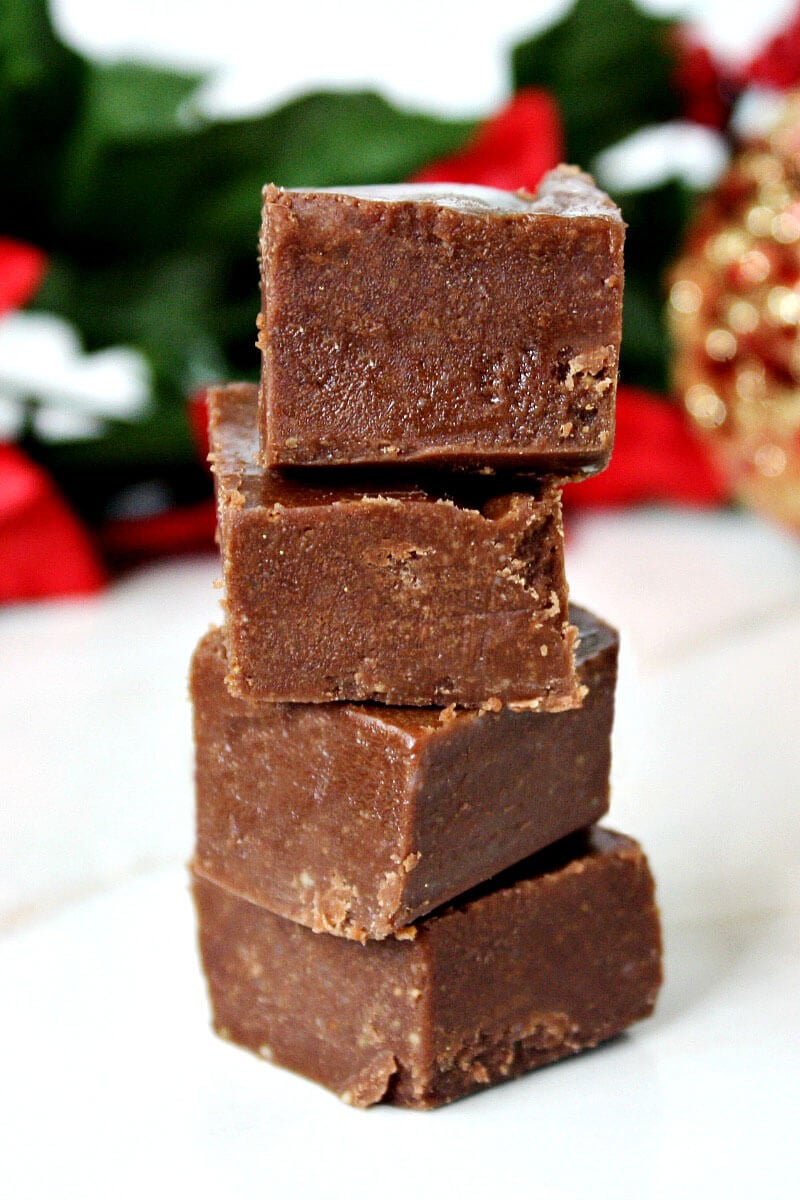 Stack of 4 Gluten-Free Vegan No-Cook Healthy Holiday Fudge squares on a white marble surface with Christmas decorations in the background