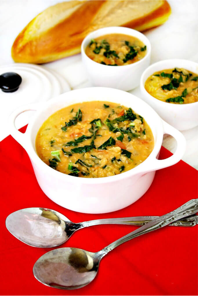 White soup bowl filled with lentil soup on a red cloth napkin next to two silver spoons