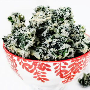 Horizontal image of a decorative red and white bowl filled with habanero kale chips on a solid white background