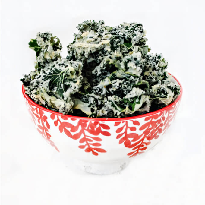 Square image of a decorative red and white bowl filled with habanero kale chips on a solid white background