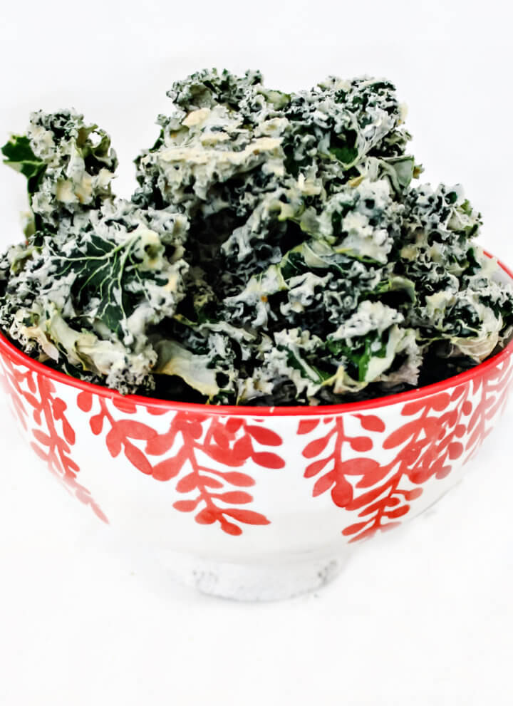 Square image of a decorative red and white bowl filled with habanero kale chips on a solid white background