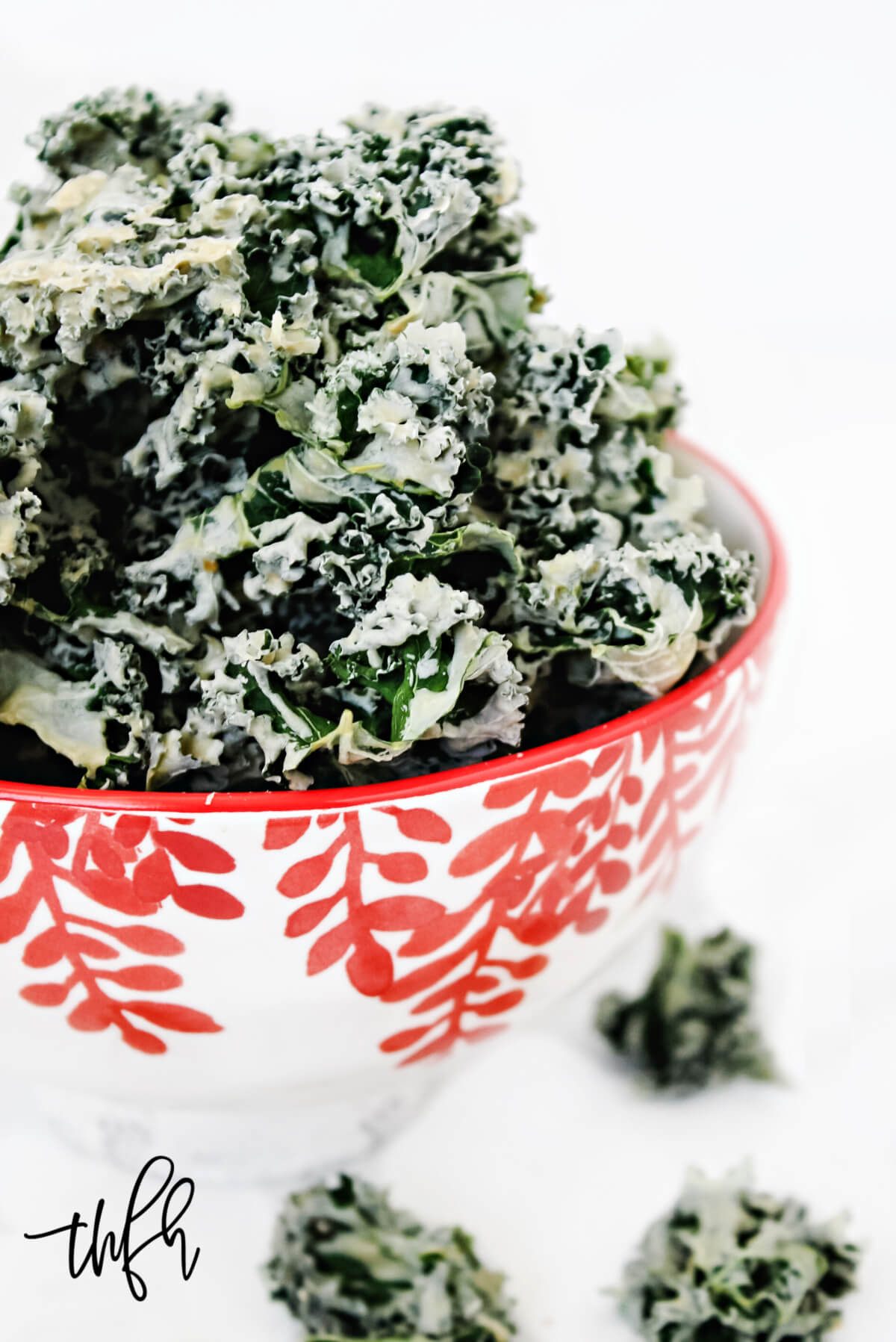 Vertical close-up image of a decorative red and white bowl filled with habanero kale chips on a solid white background