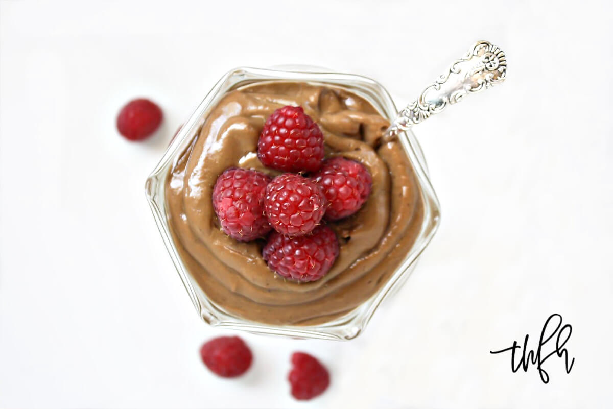 Overhead image of a glass dish filled with chocolate pudding topped with multiple raspberries with a silver spoon inserted