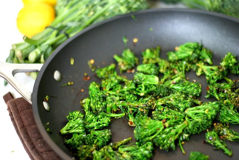 Close-up image of a skillet with Gluten-Free Vegan Spicy Sauteed Broccolini with lemons in the background