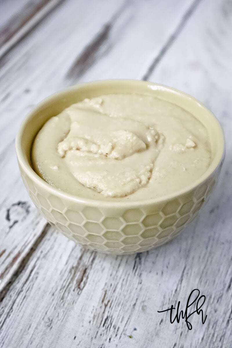 Vertical image of a cream bowl filled with The BEST Homemade Tahini on a weathered wood surface
