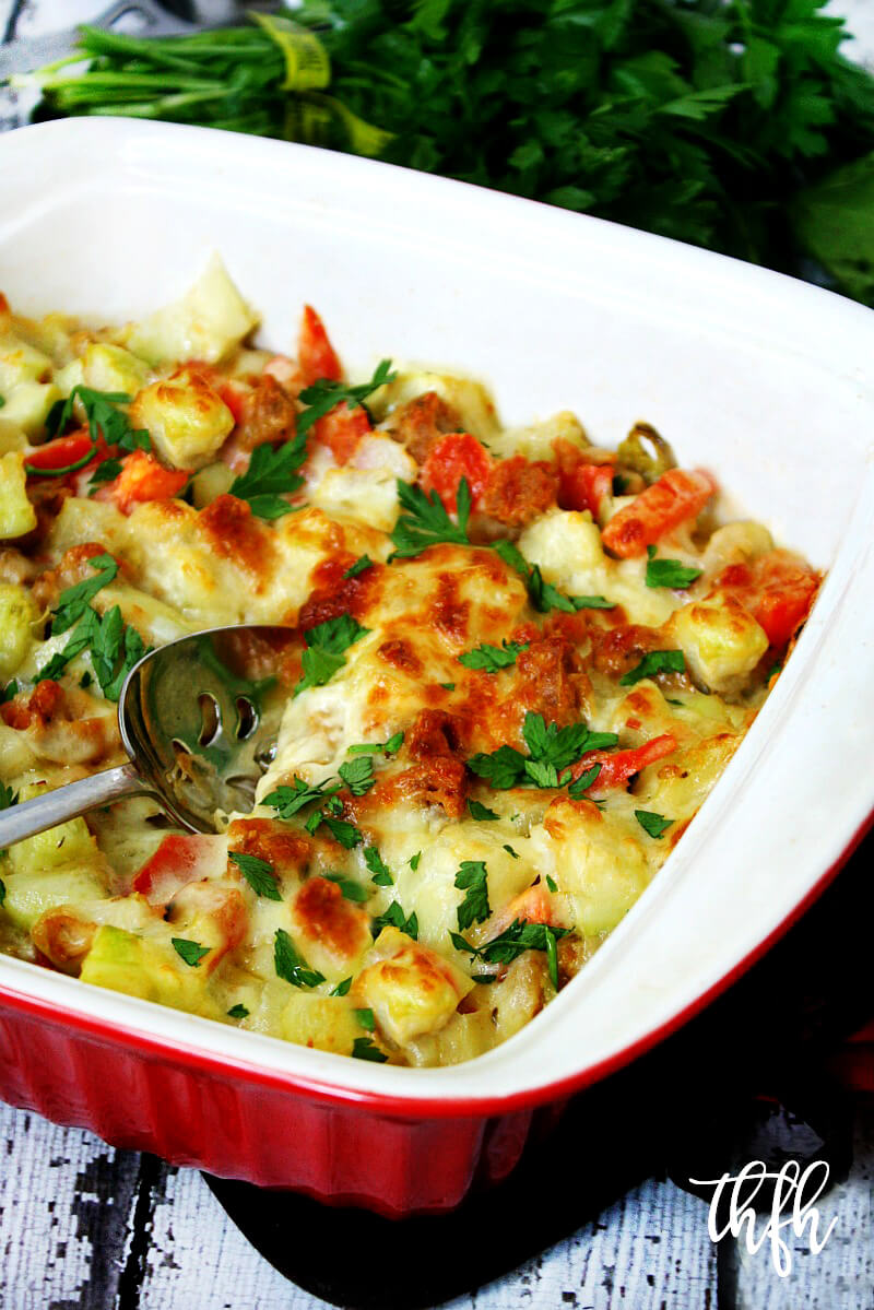 A red casserole dish filled with Spicy Vegan Italian Cucuzza Squash Casserole Bake on a white weathered wooden surface