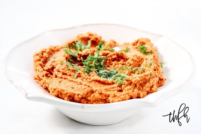 A decorative white bowl filled with Gluten-Free Vegan Smoky Chipotle Pumpkin Hummus centered in the image on a solid white background