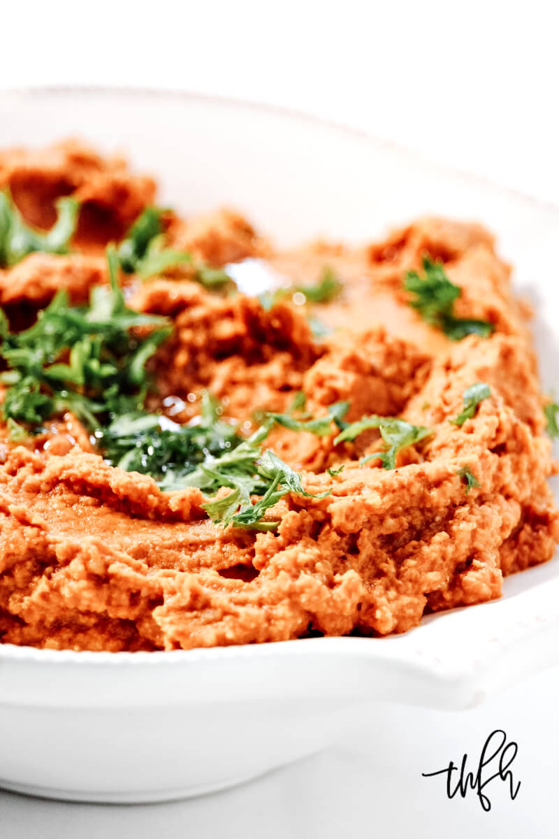 A close-up image of a white bowl filled with Gluten-Free Vegan Smoky Chipotle Pumkin Hummus garnished with chopped parsley