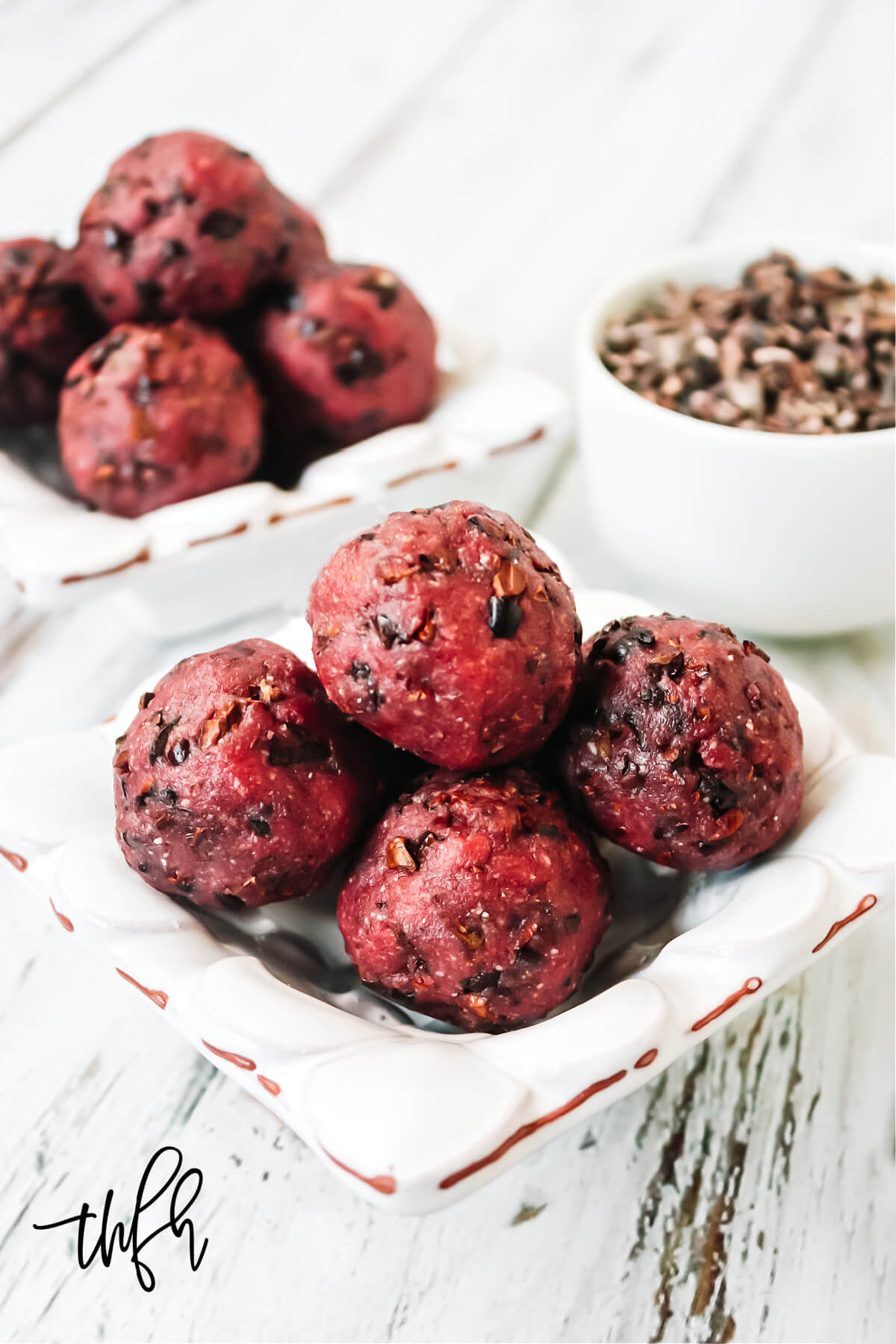 Vertical image of four red truffles in a small decorative bowl on a weathered wood background