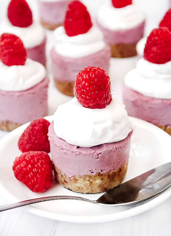 Vertical image of a Gluten-Free Vegan No-Bake Raspberry Mini Cheesecake on a white saucer with silver spoon