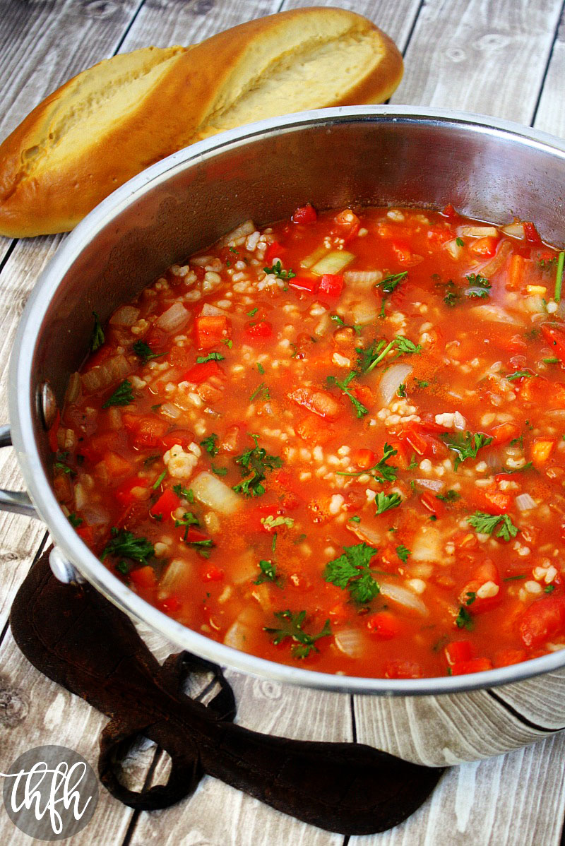 Vertical image of The BEST Vegan Stuffed Pepper Soup in a stainless steel pot on a faded wooden surface with a loaf of bread in the background 