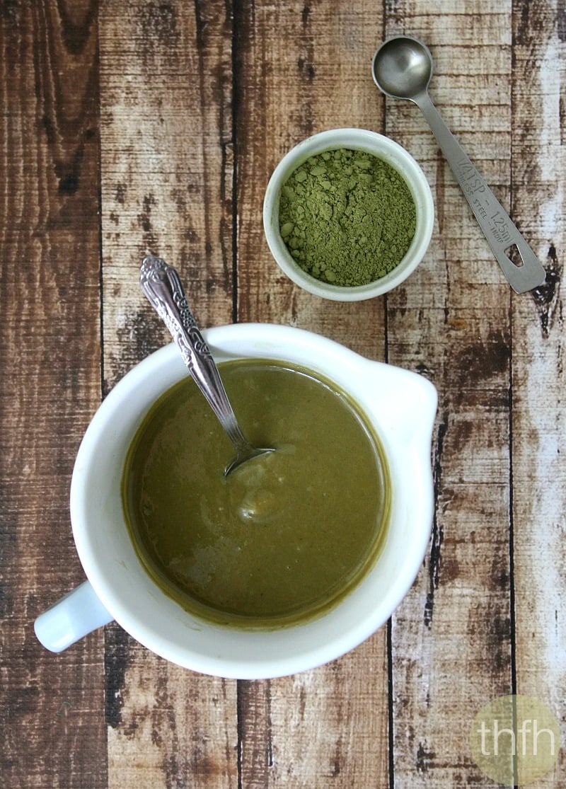Overhead vertical image of a small mixing bowl filled with Sweet Tahini and Matcha Spread on a weathered wooden surface with a small bowl of match powder next to it