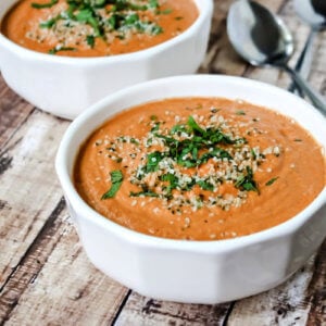 Horizontal image of two white bowls filled with tomato basil soup on a weathered wooden surface