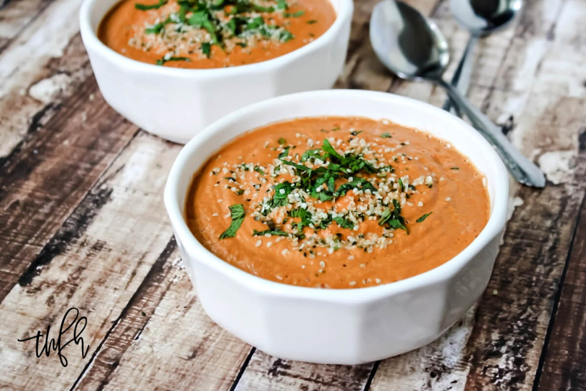 Horizontal image of two white bowls filled with tomato basil soup on a weathered wooden surface